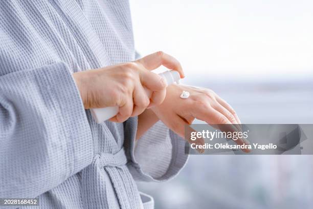 woman in bathrobe dripping essential oil on hand. aroma oil in a small glass amber bottle with craft label. - retinol stock pictures, royalty-free photos & images