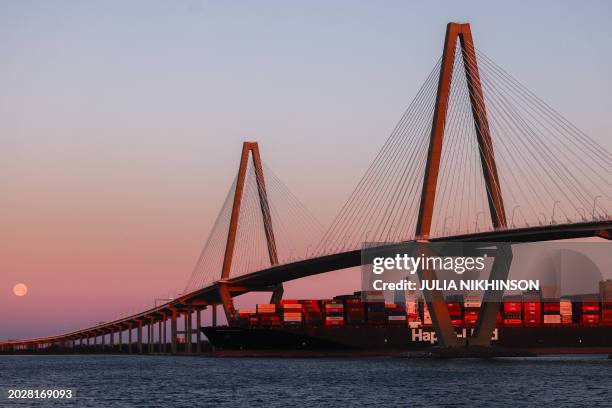 Full moon sets as a container ship passes under the Arthur Ravenel Jr. Bridge in Mount Pleasant, South Carolina, on February 24, 2024.