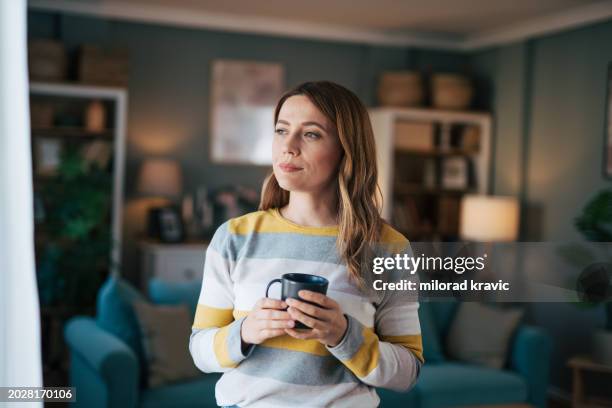 mature woman looks out the window and drinks coffee. - door het raam kijken stockfoto's en -beelden