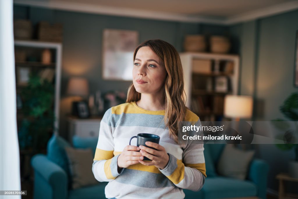 Mature woman looks out the window and drinks coffee.