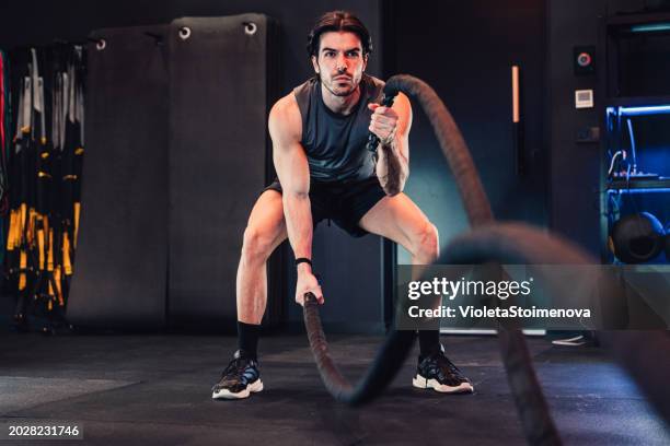 young man practicing battle rope in gym. - battle ropes stock pictures, royalty-free photos & images