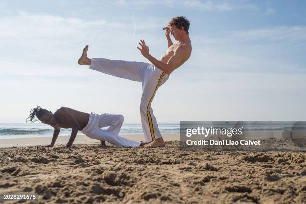 two men practicing capoeira in the beach - kicking sand stock pictures, royalty-free photos & images