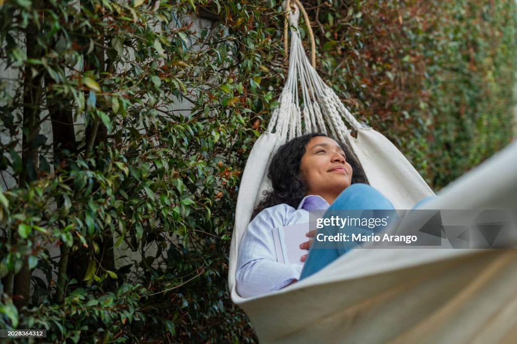 Latin woman enjoying the outdoors in the garden while on top of her hammock having a moment of reflection alone