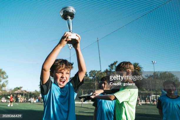 niño levantando la copa de campeones de fútbol - competición de fútbol fotografías e imágenes de stock