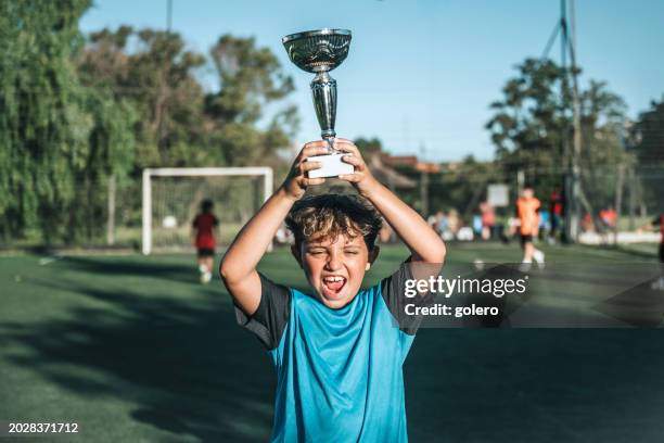 boy lifting up soccer winner cup - competição de futebol imagens e fotografias de stock