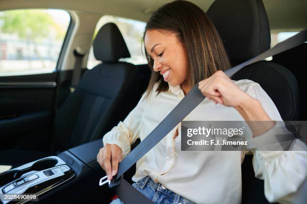woman putting on seat belt in car - cinturón de seguridad fotografías e imágenes de stock