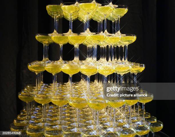 February 2024, Berlin: Many glasses filled with champagne are piled up to form a champagne pyramid at a party in Berlin-Friedrichshain. Photo:...