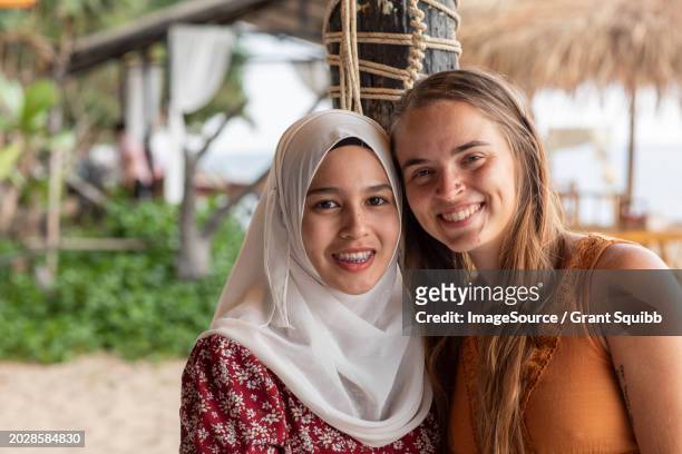 smiling portrait of two female best friends, one is wearing a hijab in a beach resort in southern thailand - tooth bonding stock pictures, royalty-free photos & images