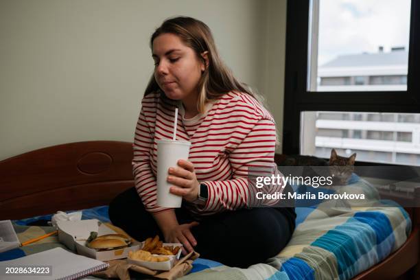 thoughtful young woman with a drink and fast food on a bed with a cat - chicken strip stock pictures, royalty-free photos & images