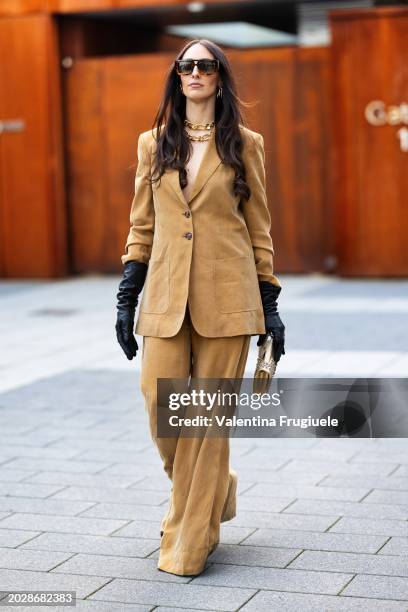 Elisa Taviti is seen wearing tortoise shell sunglasses, gold chain necklaces, gold hoop earrings, black leather gloves and a beige suede suit outside...