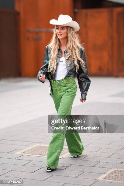 Emili Sindlev wears a white cowboy hat, a black gathered leather jacket , a white t-shirt from Miu Miu, green denim / jeans flared pants, black and...