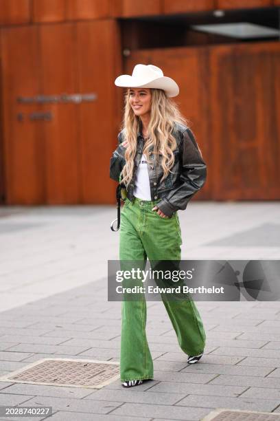 Emili Sindlev wears a white cowboy hat, a black gathered leather jacket , a white t-shirt from Miu Miu, green denim / jeans flared pants, black and...