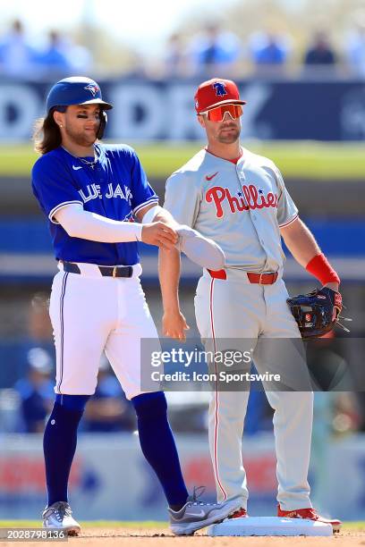 Toronto Blue Jays shortstop Bo Bichette smiles as Philadelphia Phillies infielder Whit Merrifield looks on during the spring training game between...