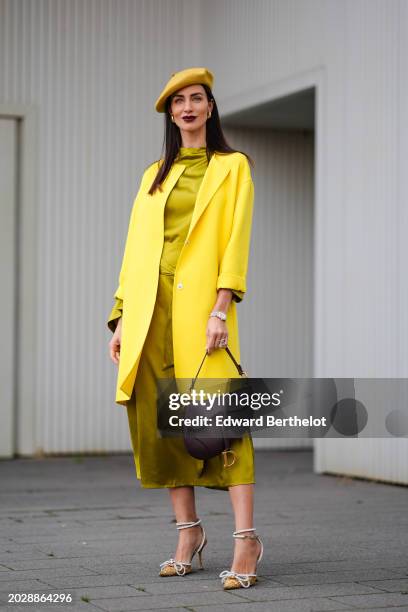 Guest wears a yellow beret hat, a yellow oversized jacket , a khaki lustrous shiny silk dress, a brown leather Dior Saddle bag, pointed golden shiny...
