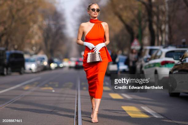 Leonie Hanne wears sunglasses, a red gathered sleeveless dress, a white gloves, a brown and white leather Fendi bag, outside Fendi, during the Milan...