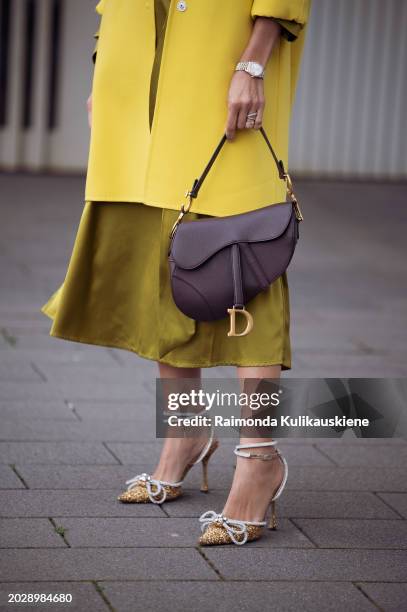 Guest wears a yellow jacket, a khaki green shiny silk dress, a brown leather Dior Saddle bag, pointed golden shiny shoes with crystal details outside...