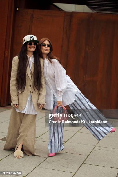 Angela Rozas Saiz wears a blue and white NY baseball hat, a long white shirt, black sunglasses, puffy light beige sandals, and a linen beige...