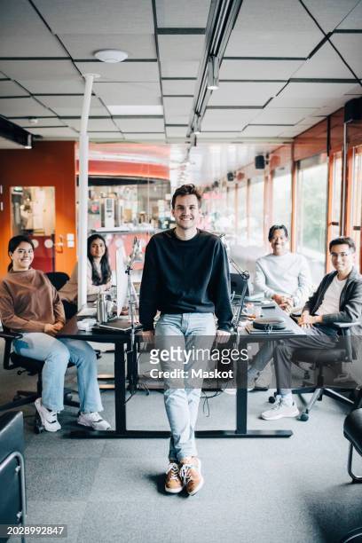 portrait of smiling male entrepreneur leaning at desk with team sitting in office - happy programmer stock pictures, royalty-free photos & images