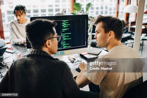 rear view of male programmers discussing while doing coding on computer at office - computer code stock pictures, royalty-free photos & images