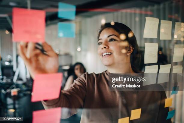 smiling female business professional explaining during brainstorming session at office seen through glass - vanguardista fotografías e imágenes de stock