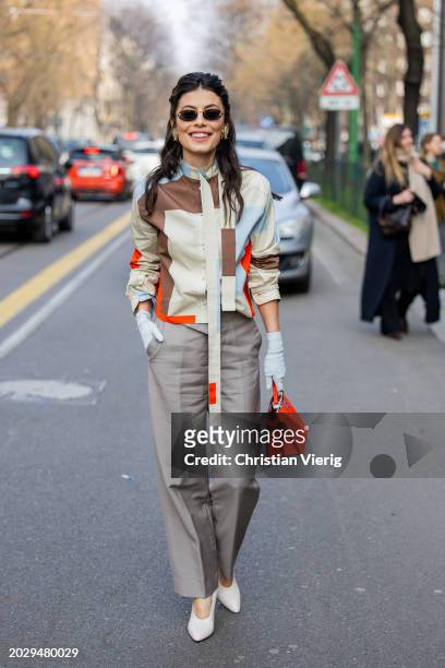 Guest wears grey pants, red bag, white gloves, beige brown turquoise jacket outside Fendi during the Milan Fashion Week - Womenswear Fall/Winter...