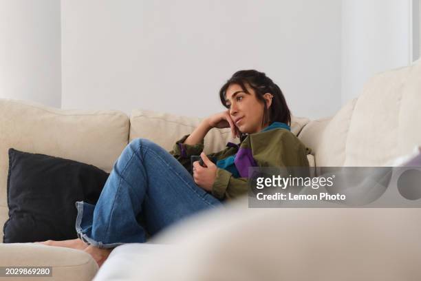 medium shot of a carefree and authentic generation z latino female taking a break sitting on a confortable sofa taking some hot drink at home on a sunny day - confortable imagens e fotografias de stock