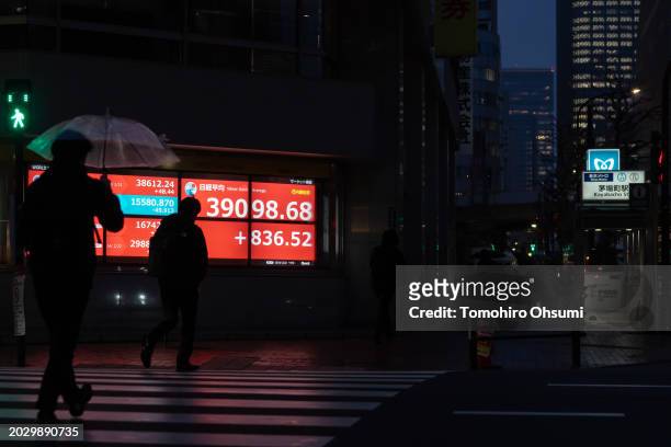 Pedestrians walk in front of an electronic board displaying the closing figure of the Nikkei Stock Average on February 22, 2024 in Tokyo, Japan. The...