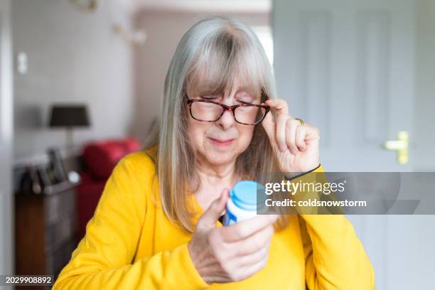 senior woman taking prescription medicine at home - acetylsalicylizuur stockfoto's en -beelden