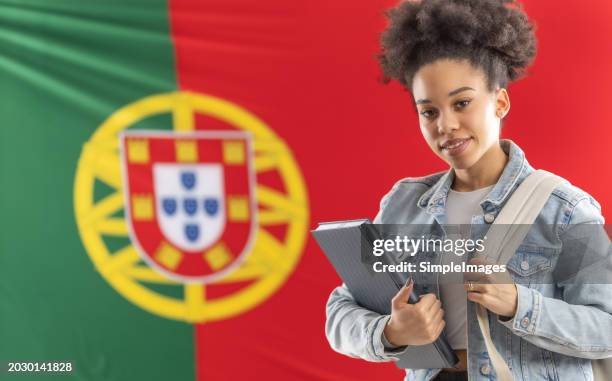 african american student of portuguese language standing in front of portuguese flag and holding textbooks. - white flag stock pictures, royalty-free photos & images