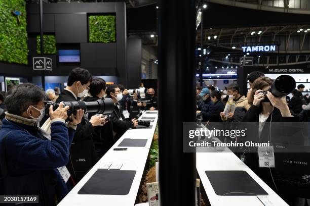 Visitors try out mirrorless digital cameras mounted with tele-photo lenses in the OM System booth during the CP+ 2024 show on February 22, in...