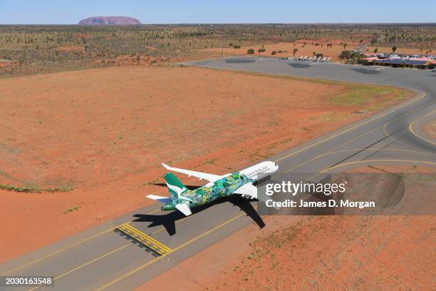 An aerial image of an Airbus A220 for QantasLink passing Uluru situated within Uluru-Kata Tjuta National Park on February 22, 2024 in Uluru,...