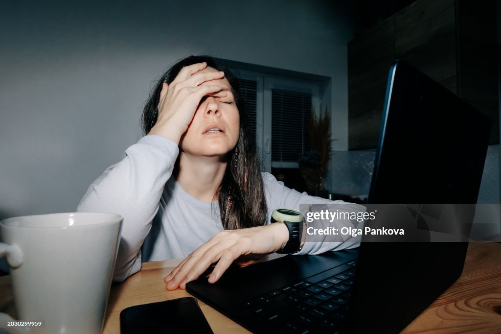 Tired and upset midl-aged woman works in a home office at night