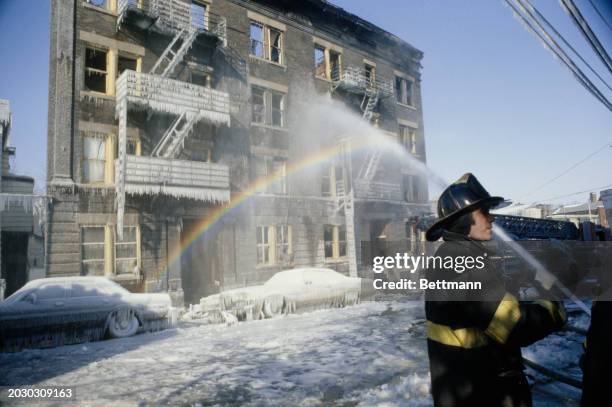Plumes of spray from a firefighter's hose form a rainbow and icicles during freezing weather conditions in Yonkers, New York, February 9th 1979....