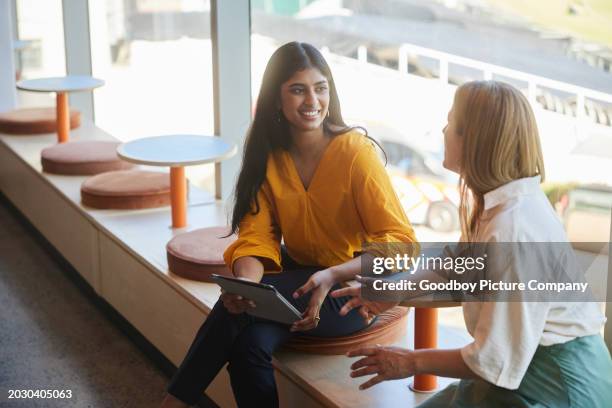 smiling diverse businesswomen sitting at an office table and talking over a tablet - entrepreneur stockfoto's en -beelden