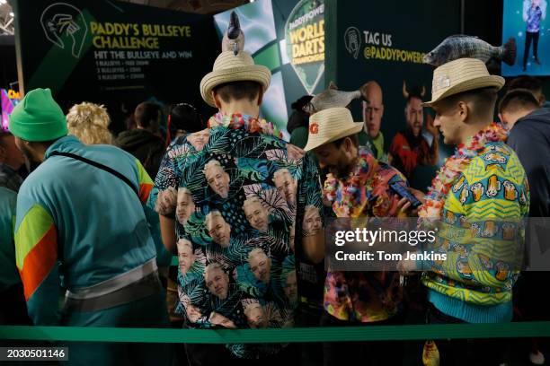 Spectators dressed with a Hawaiian shirt featuring the player Peter Wright and fish on hats in the fan village before play starts during day one of...