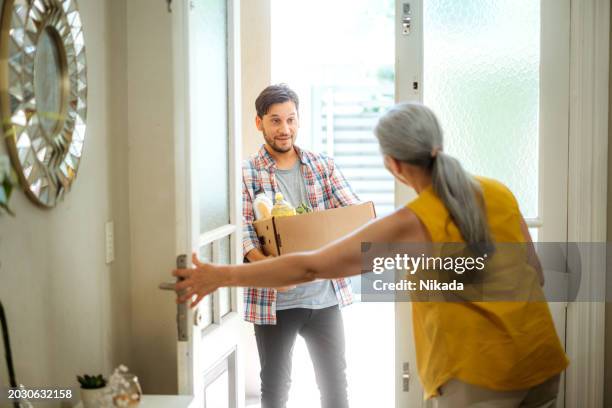 junger mann liefert lebensmittel an ältere frau zu hause - hauszustellung stock-fotos und bilder