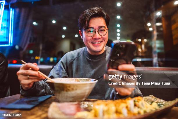 cheerful asian man using smart phone while enjoying meal in a local japanese restaurant - chinese noodles stock pictures, royalty-free photos & images