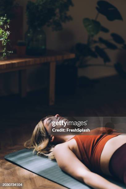 young woman relaxing on yoga mat in serene home environment - sleep hygiene stock pictures, royalty-free photos & images