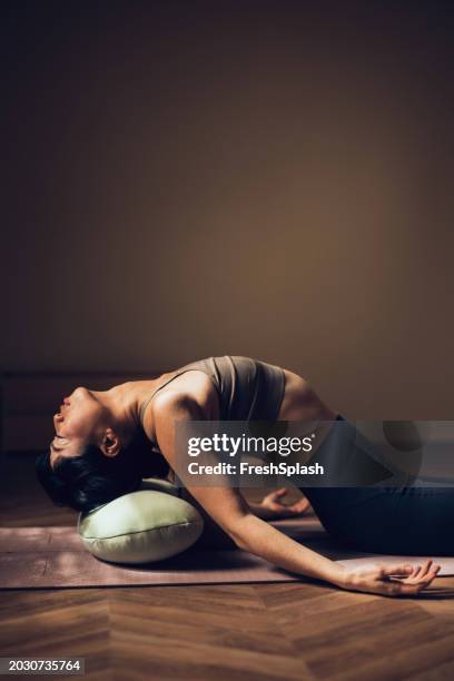focused woman practicing yoga pose on mat with bolster indoors - cushion stock pictures, royalty-free photos & images