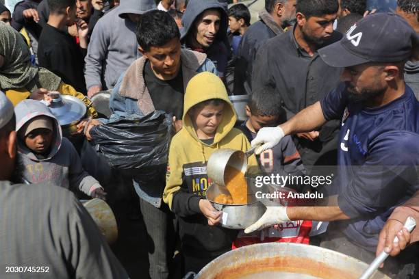 Palestinians, including women and children, receive food after waiting in a line for food, distributed by charity organizations, since they are...