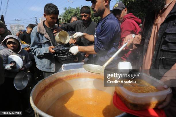 Palestinians, including women and children, receive food after waiting in a line for food, distributed by charity organizations, since they are...