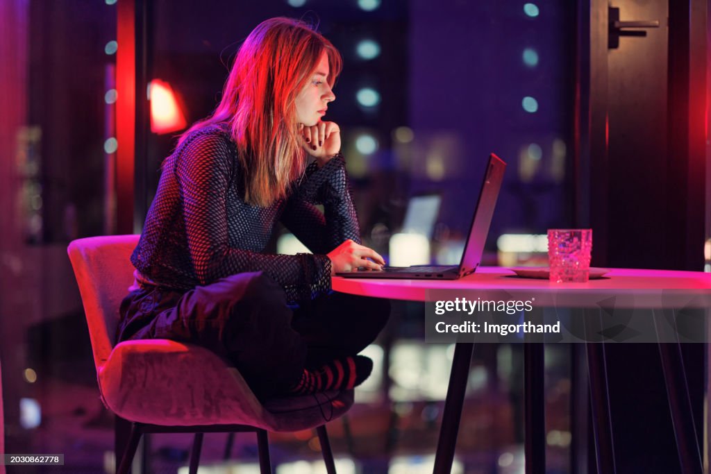 Teenage girl using laptop in a modern city apartment at night