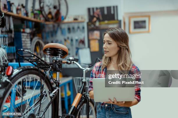 female bicycle shop mechanic using laptop - reparatiewerkplaats stockfoto's en -beelden