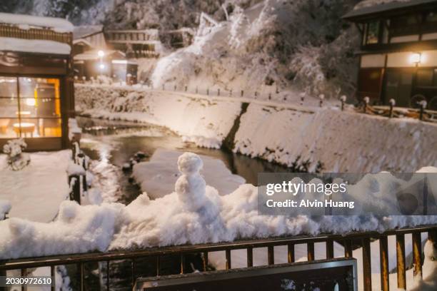 a small snowman stands by the bridge of ginzan river on a snowy night in the ginzan onsen area of oishida city, yamagata prefecture, japan. - smokey mountain spring stock pictures, royalty-free photos & images