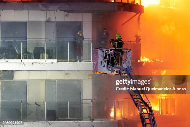 Two people take shelter from the fire on one of the terraces of the burning building on February 22, 2024 in Valencia, Spain. A large fire has swept...