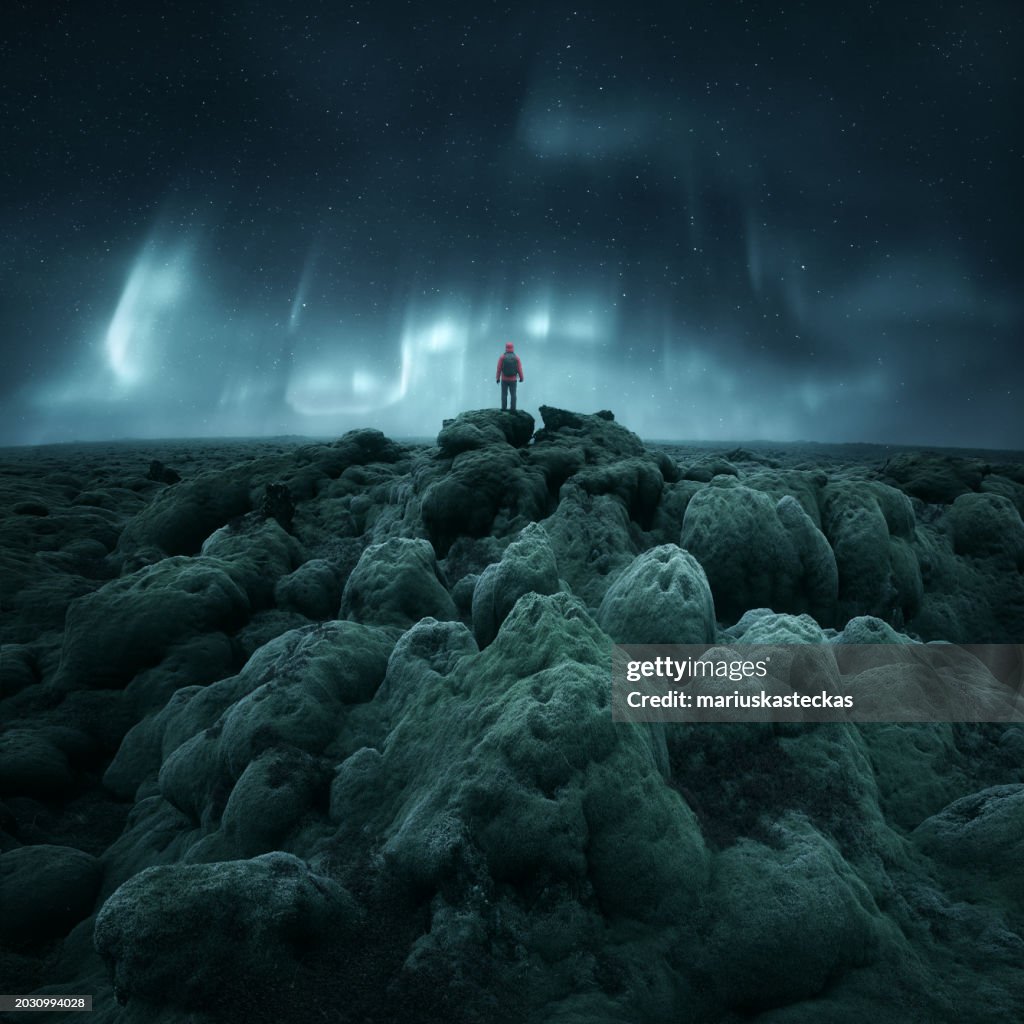 Distant silhouette of a person standing on rocks below Northern Lights (Aurora borealis), Iceland