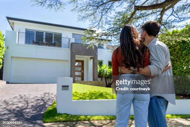 glückliches paar steht vor seinem neuen zuhause. beide tragen freizeitkleidung und umarmen sich. rückansicht. - home renovations australia stock-fotos und bilder