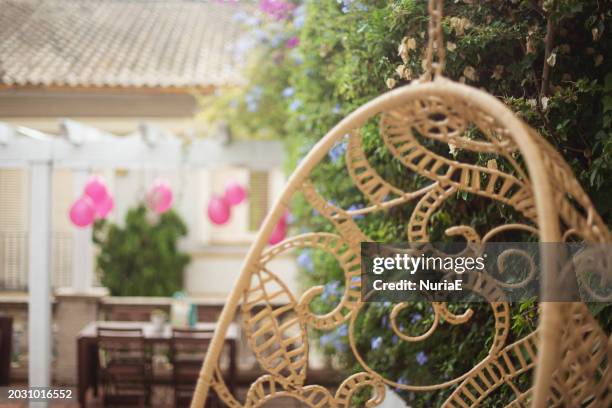 close-up of a hanging chair in a garden with pink balloons hanging on a pergola in background - nuria stock pictures, royalty-free photos & images