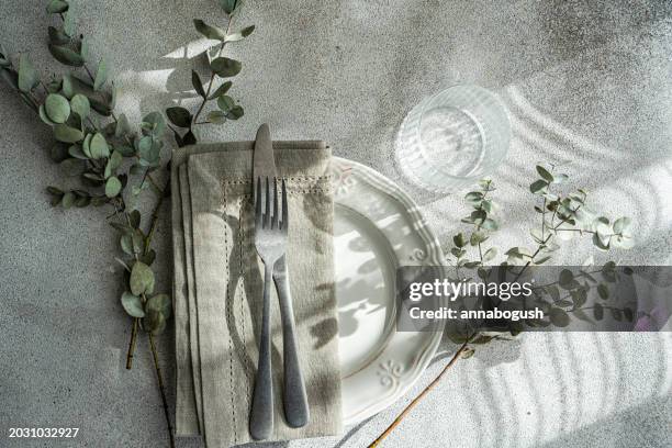 overhead view of a rustic place setting on a table in sunlight with eucalyptus leaves - rustic dinner party stock pictures, royalty-free photos & images