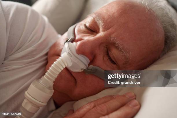 uomo maturo che dorme con una macchina cpap (pressione positiva continua delle vie aeree) dopo essere stato diagnosticato con apnea notturna - attrezzatura per la respirazione artificiale foto e immagini stock